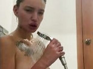 A wet girl with tattoos is having fun in the shower.